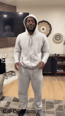 A Man In A White Hoodie Is Standing In A Living Room GIF