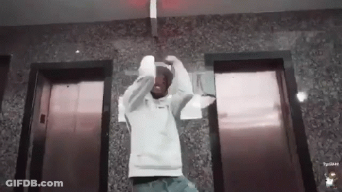 Man In White Hoodie In Front Of Elevators GIF