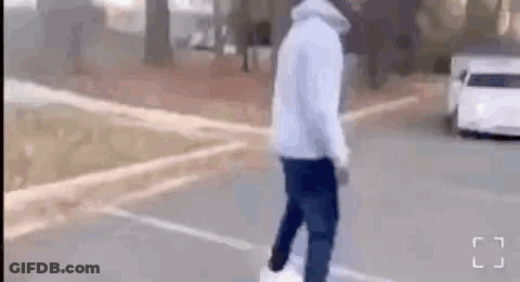 A Man In A White Hoodie Is Walking Down A Street Next To A Car . GIF