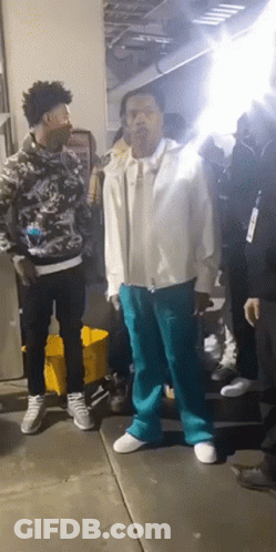 A Man In A White Jacket And Blue Pants Is Standing In A Crowd Of People GIF