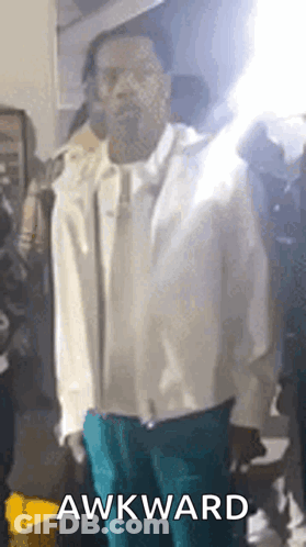 A Man In A White Jacket And Blue Pants Is Standing In Front Of A Crowd With The Word Awkward On The Bottom . GIF