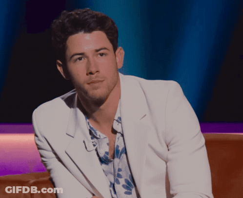 A Man In A White Jacket And Floral Shirt Is Sitting On A Brown Couch GIF