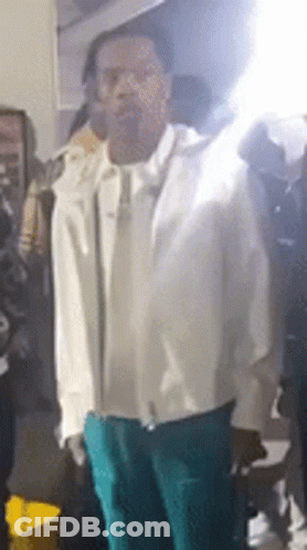 A Man In A White Jacket And Green Pants Is Standing In Front Of A Crowd Of People . GIF