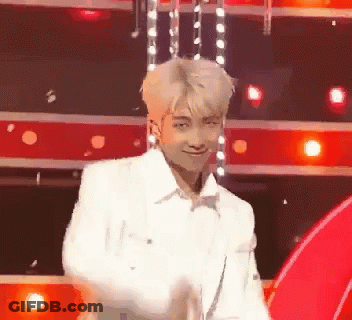 A Man In A White Jacket Is Dancing On A Stage In Front Of Red Lights . GIF