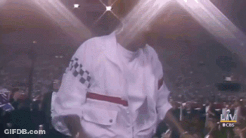A Man In A White Jacket Is Dancing On Stage In Front Of A Crowd . GIF