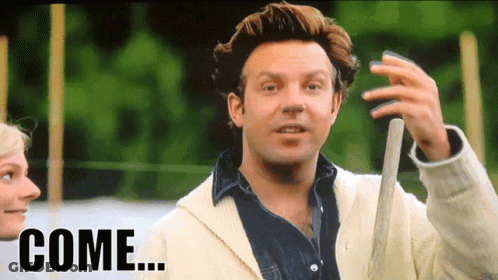 A Man In A White Jacket Is Holding A Baseball Bat And The Word Come Is On The Screen Behind Him GIF