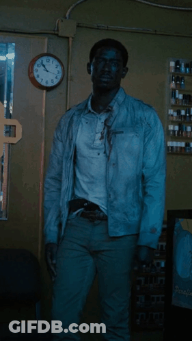 A Man In A White Jacket Is Standing In Front Of A Clock That Shows The Time As 11:55 GIF