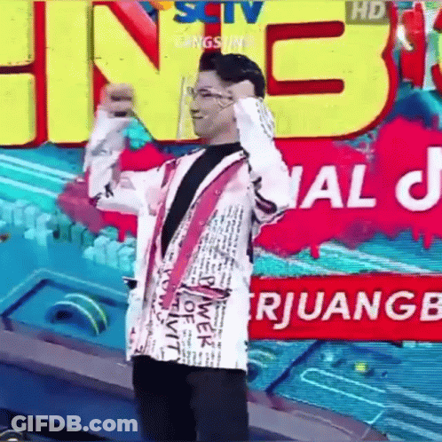 A Man In A White Jacket Is Standing In Front Of A Large Sign That Says ' Sctv ' On It . GIF