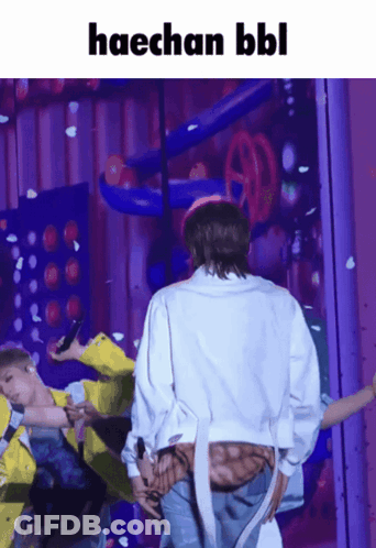 A Man In A White Jacket Is Standing In Front Of A Purple Wall With The Words Haechan Bbl Written Above Him GIF
