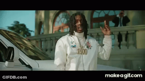 A Man In A White Jacket Is Standing In Front Of A White Car And Making A Peace Sign . GIF