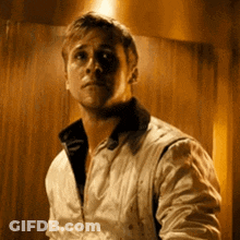 A Man In A White Jacket Is Standing In Front Of A Wooden Wall In A Dark Room . GIF