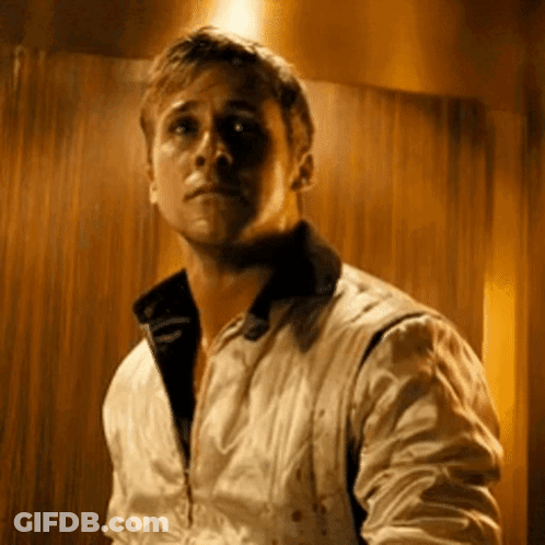 A Man In A White Jacket Is Standing In Front Of A Wooden Wall Looking At The Camera . GIF