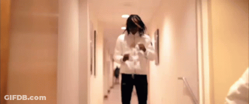 A Man In A White Jacket Is Walking Down A Hallway With Stairs . GIF