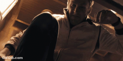 A Man In A White Jacket Sits On The Floor Looking Down GIF