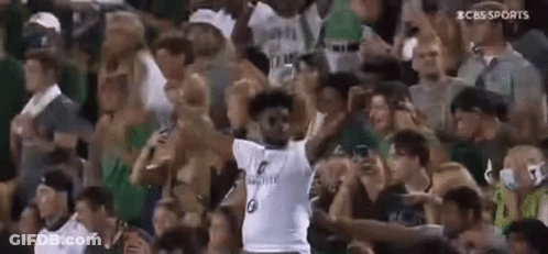 A Man In A White Jersey Is Standing In Front Of A Crowd . GIF