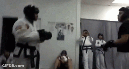 A Man In A White Karate Uniform Is Fighting Another Man In A Black Belt In A Room . GIF