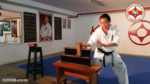 A Man In A White Karate Uniform Is Standing In Front Of A Sign That Says Dojo Oliver GIF