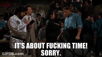 A Man In A White Karate Uniform Is Talking To A Man In A Black Belt In A Crowd Of People . GIF