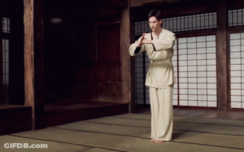 A Man In A White Karate Uniform Stands In A Room With Sliding Glass Doors GIF