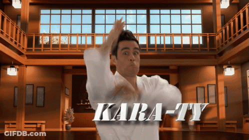 A Man In A White Karate Uniform Stands In Front Of A Sign That Reads Kara-Ty GIF