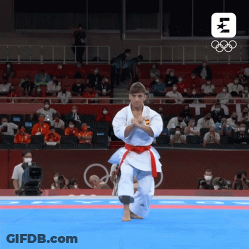 A Man In A White Karate Uniform With A Red Belt Performs A Karate Move In Front Of A Crowd At The Olympics GIF