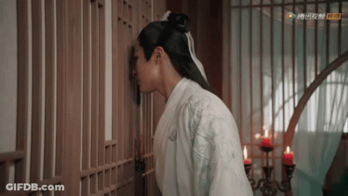 A Man In A White Kimono Is Leaning Against A Wooden Fence . GIF