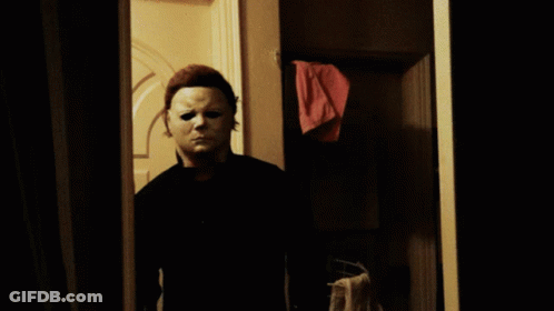 A Man In A White Mask Is Standing In A Doorway Holding A Knife GIF