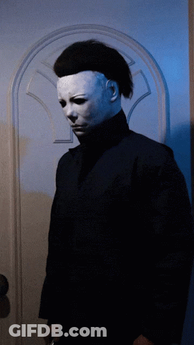 A Man In A White Mask Stands In Front Of A Blue Door GIF
