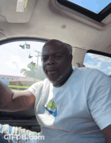 A Man In A White Nike Shirt Is Sitting In A Car GIF
