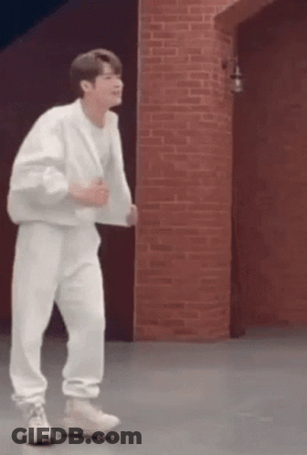 A Man In A White Outfit Is Dancing In Front Of A Brick Wall . GIF