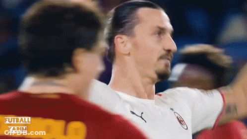 A Man In A White Puma Shirt Stands Next To Another Man GIF