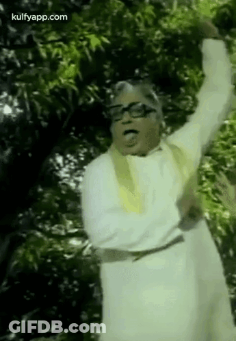 A Man In A White Robe And Glasses Is Standing In Front Of A Tree With His Arms In The Air . GIF