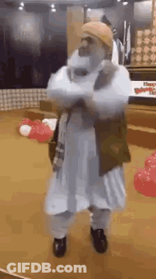 A Man In A White Robe And Hat Is Dancing In A Room . GIF