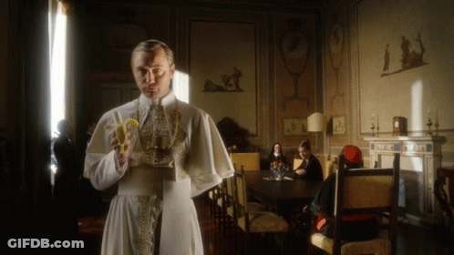A Man In A White Robe Holds A Banana In A Room GIF