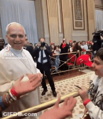 A Man In A White Robe Is Shaking Hands With A Boy In A Red Hat In Front Of A Crowd . GIF