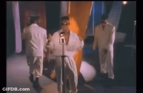 A Man In A White Robe Is Singing Into A Microphone While Standing Next To Two Other Men In Suits . GIF