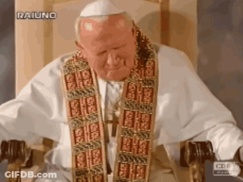 A Man In A White Robe Is Sitting In A Chair With A Cbs Logo Behind Him GIF