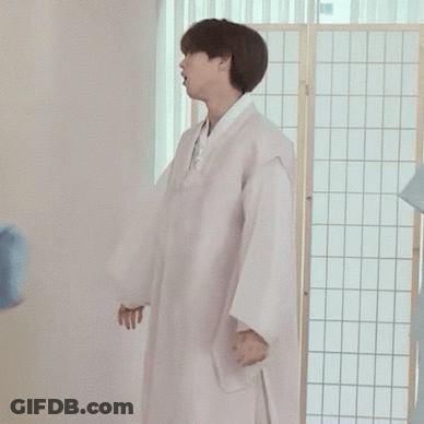 A Man In A White Robe Is Standing In Front Of A Room Divider Holding A Blue Shirt . GIF