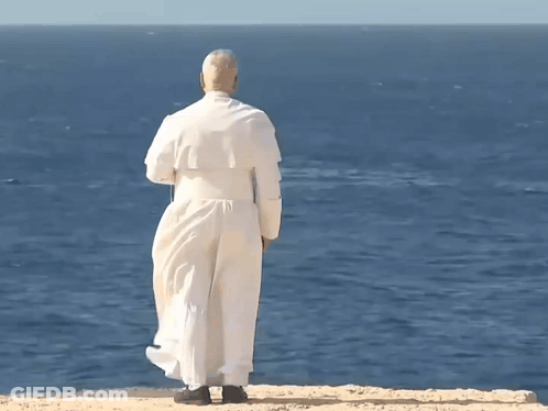A Man In A White Robe Is Standing On A Cliff Overlooking A Body Of Water GIF