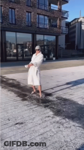 A Man In A White Robe Is Standing On A Sidewalk GIF
