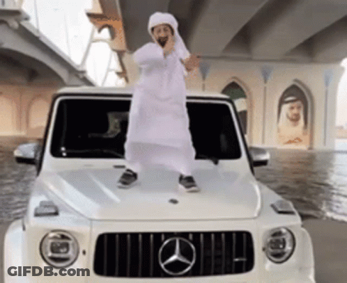 A Man In A White Robe Is Standing On The Hood Of A White Mercedes GIF