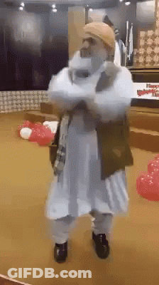 A Man In A White Robe Is Standing With His Arms Crossed In A Room With Red And White Balloons . GIF