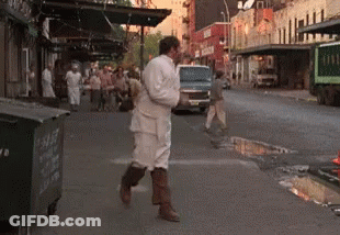 A Man In A White Robe Is Walking Down A Street GIF