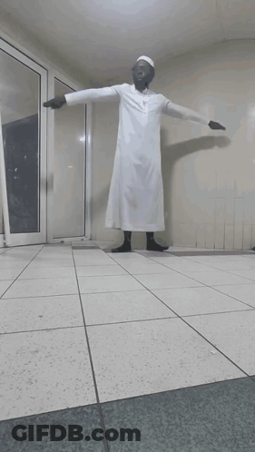 A Man In A White Robe Stands In A Hallway GIF