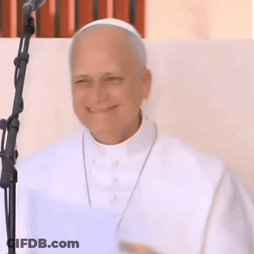 A Man In A White Robe Stands In Front Of A Microphone Smiling GIF