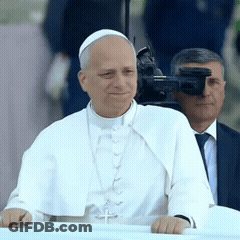 A Man In A White Robe With A Cross On His Neck GIF