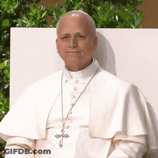 A Man In A White Robe With A Cross On His Necklace GIF