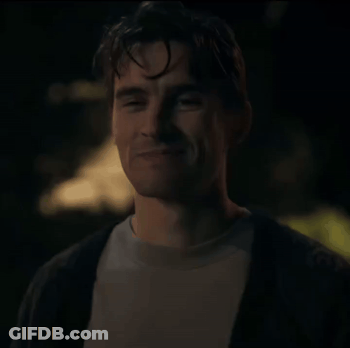 A Man In A White Shirt And A Black Cardigan Smiles At The Camera GIF