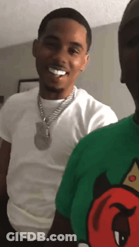 A Man In A White Shirt And A Green Shirt With A Devil On It Smiles GIF