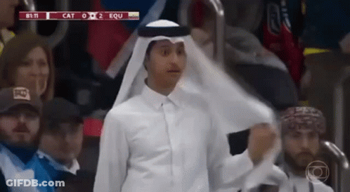 A Man In A White Shirt And A White Scarf Is Standing In A Crowd . GIF